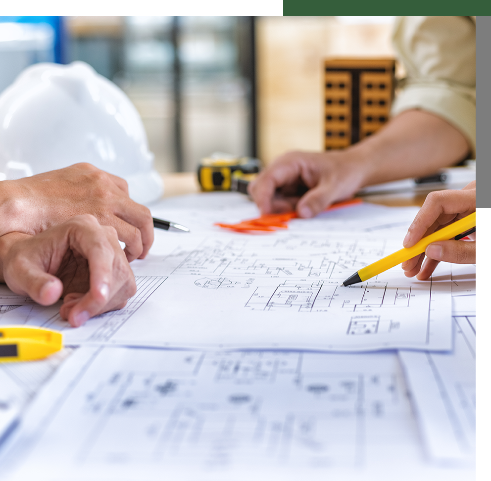Close-up of hands examining architectural blueprints on a table, with safety helmets and a miniature building in the background.